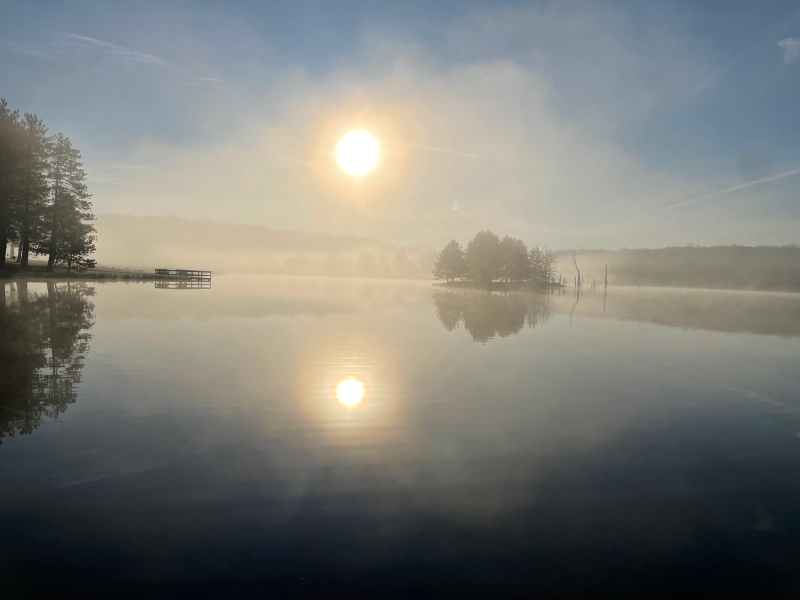 Calm lake at sunrise with mist rising, an island with tall trees reflected in still water
