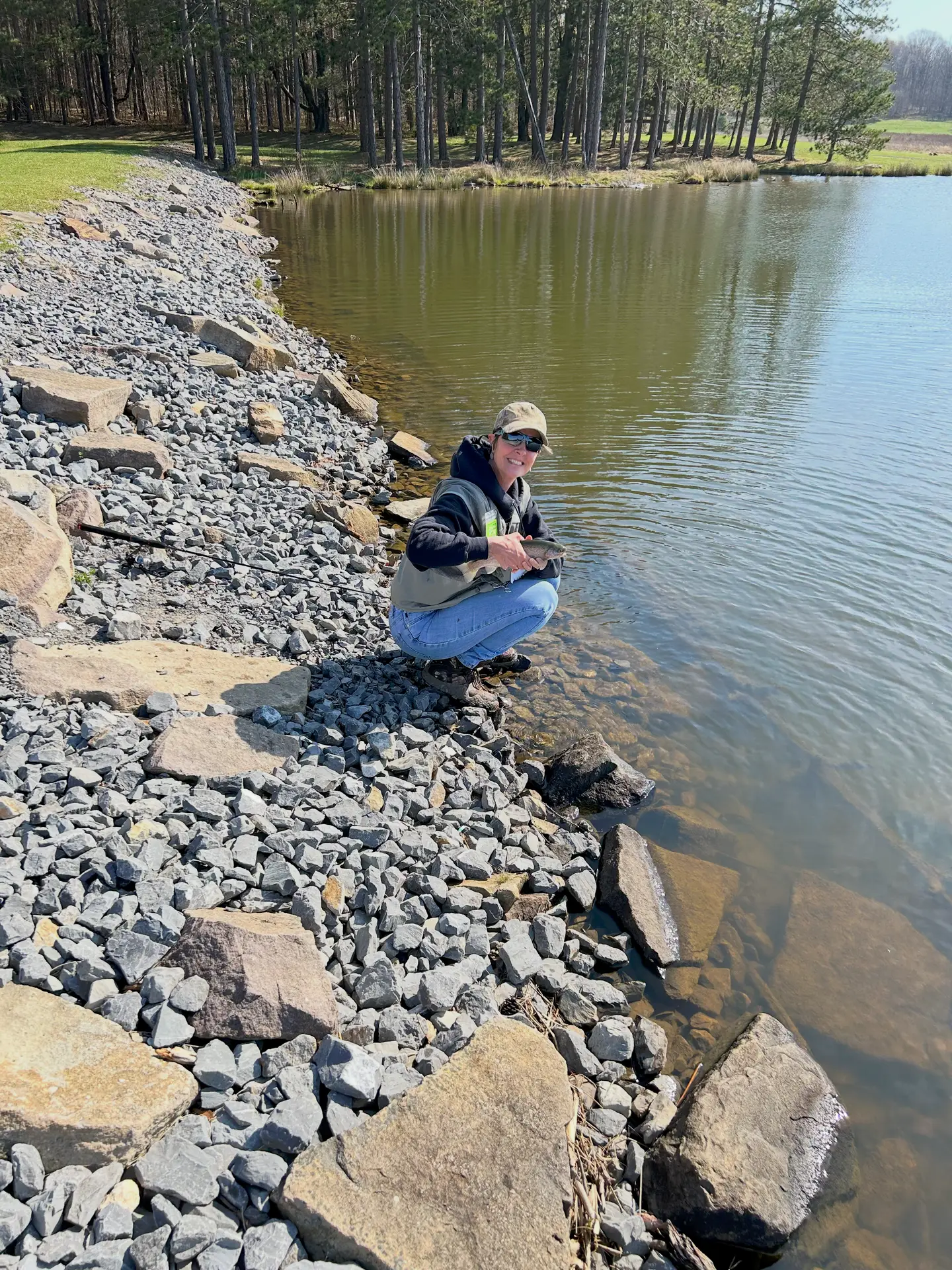 Amy Summers crouching beside a lake, holding a small trout before releasing it.